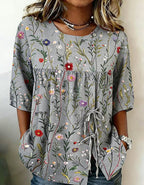 Gray tunic blouse with a colorful wildflower print, button-front detail, drawstring tie, and elbow-length sleeves.