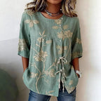 Sage green linen-blend blouse featuring cream floral embroidery, a side button placket, and tie-front detailing.