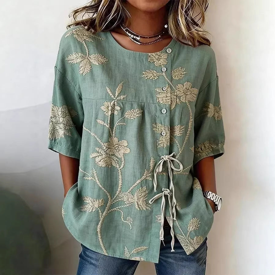 Sage green linen-blend blouse featuring cream floral embroidery, a side button placket, and tie-front detailing.