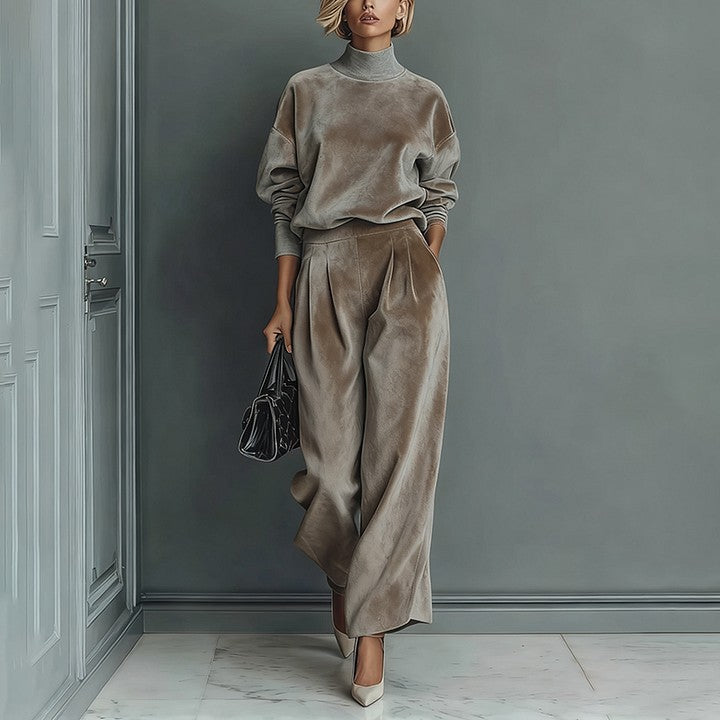 A woman wears a taupe velour high-neck long-sleeve top and matching pleated wide-leg pants against a gray wall.