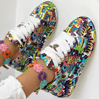 Colorful graffiti-print sneakers with white laces, worn with embroidered floral anklets on a white background.