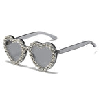 Heart-shaped sunglasses with grey lenses and a frame rimmed in sparkling clear rhinestones.