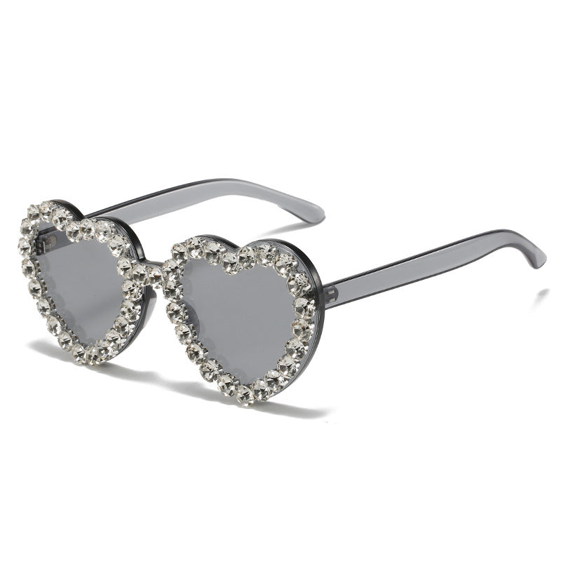 Heart-shaped sunglasses with grey lenses and a frame rimmed in sparkling clear rhinestones.