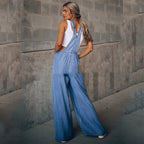 Woman in a white tank top wearing light-wash blue denim overalls with a relaxed, wide-leg fit.
