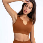A woman wears a rust-brown ribbed sports bra with a U-shaped neckline on a white background.
