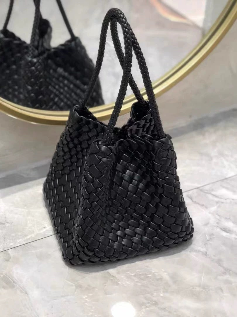 Black woven leather handbag with braided shoulder straps, reflected in a round gold-rimmed mirror.