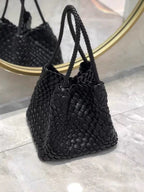 Black woven leather handbag with braided shoulder straps, reflected in a round gold-rimmed mirror.