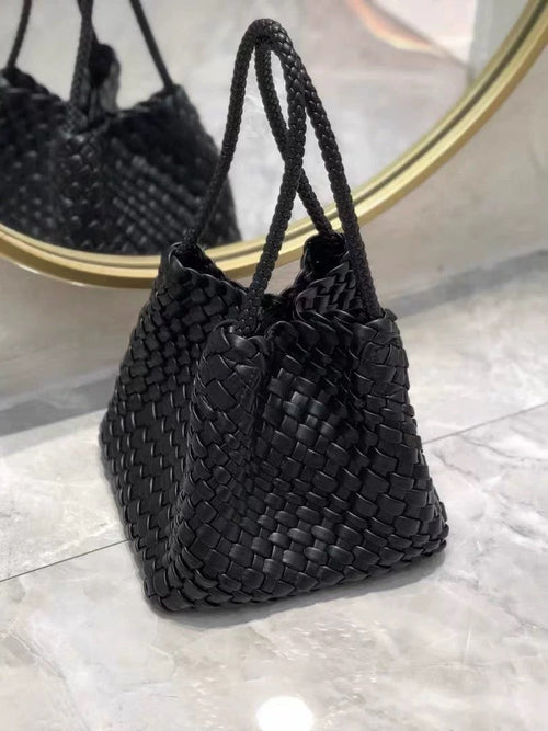 Black woven leather handbag with braided shoulder straps, reflected in a round gold-rimmed mirror.