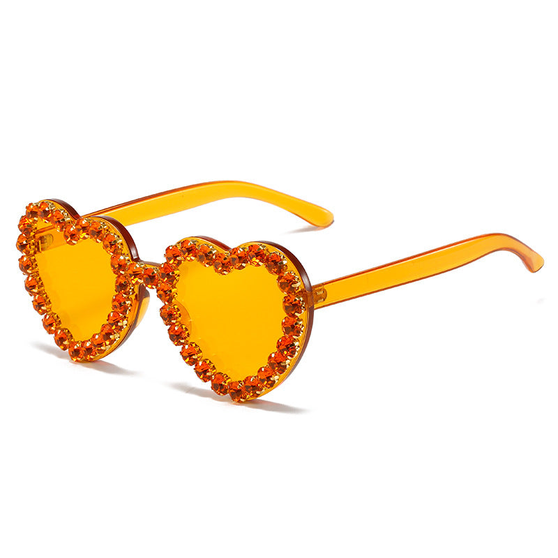 Amber-colored heart-shaped sunglasses featuring rims embellished with sparkling orange crystals.
