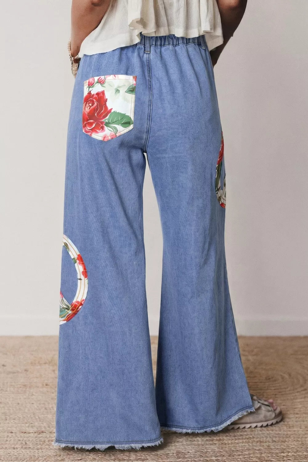 Floral peace sign wide leg jeans by Trendsi featuring a relaxed fit, floral embroidery, and a casual, trendy style.
