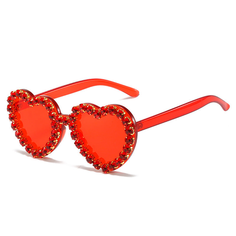 Red heart-shaped sunglasses with translucent frames and a rim of sparkling red rhinestones.