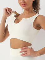 Cream-colored ribbed sports bra with a U-shaped notched neckline, featuring a cropped, sleeveless athletic design.