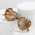 Heart-shaped sunglasses with brown tinted lenses and a gold crystal-encrusted rim, displayed on white pedestals.