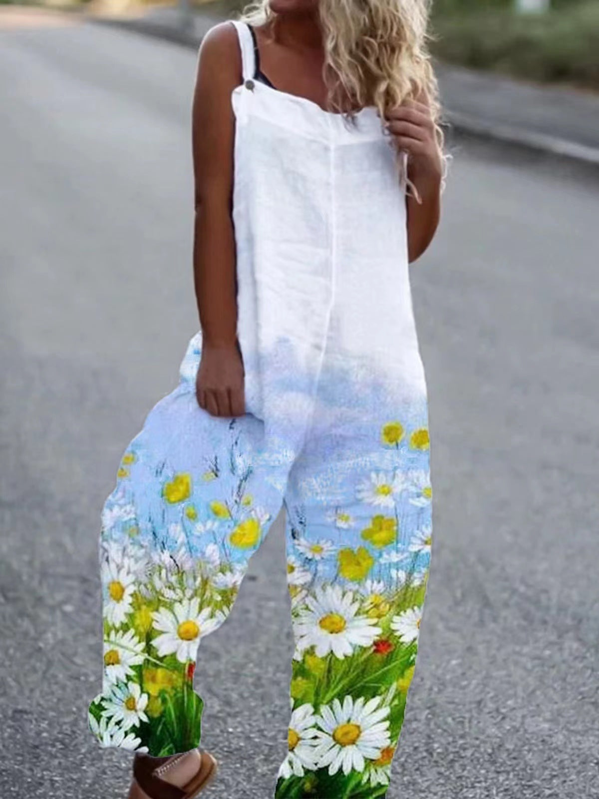 White sleeveless linen jumpsuit featuring a blue sky and meadow print with yellow and white daisy wildflowers.