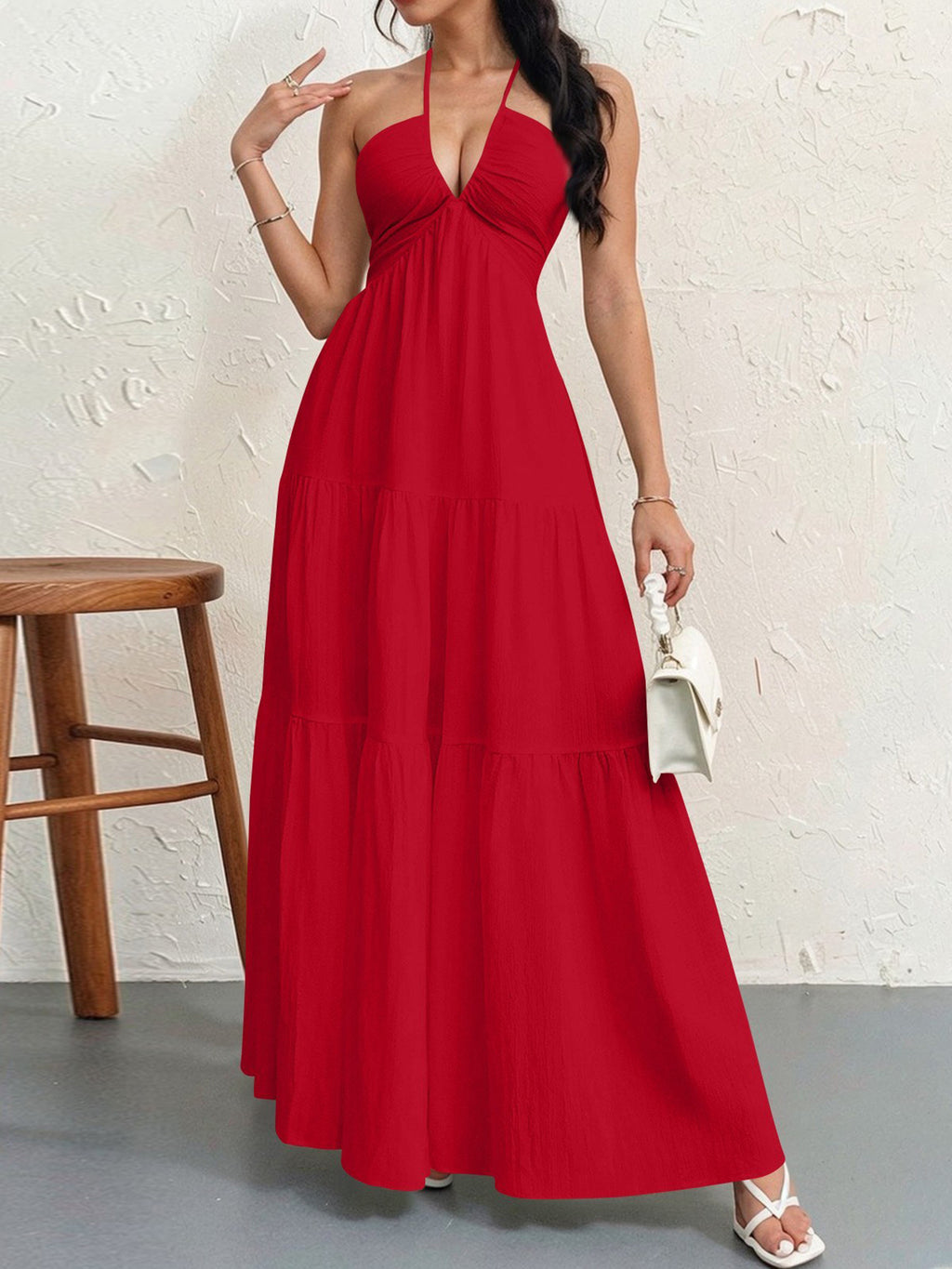 A woman wears a vibrant red, floor-length tiered maxi dress with a halter neckline and a deep, gathered V-neck.