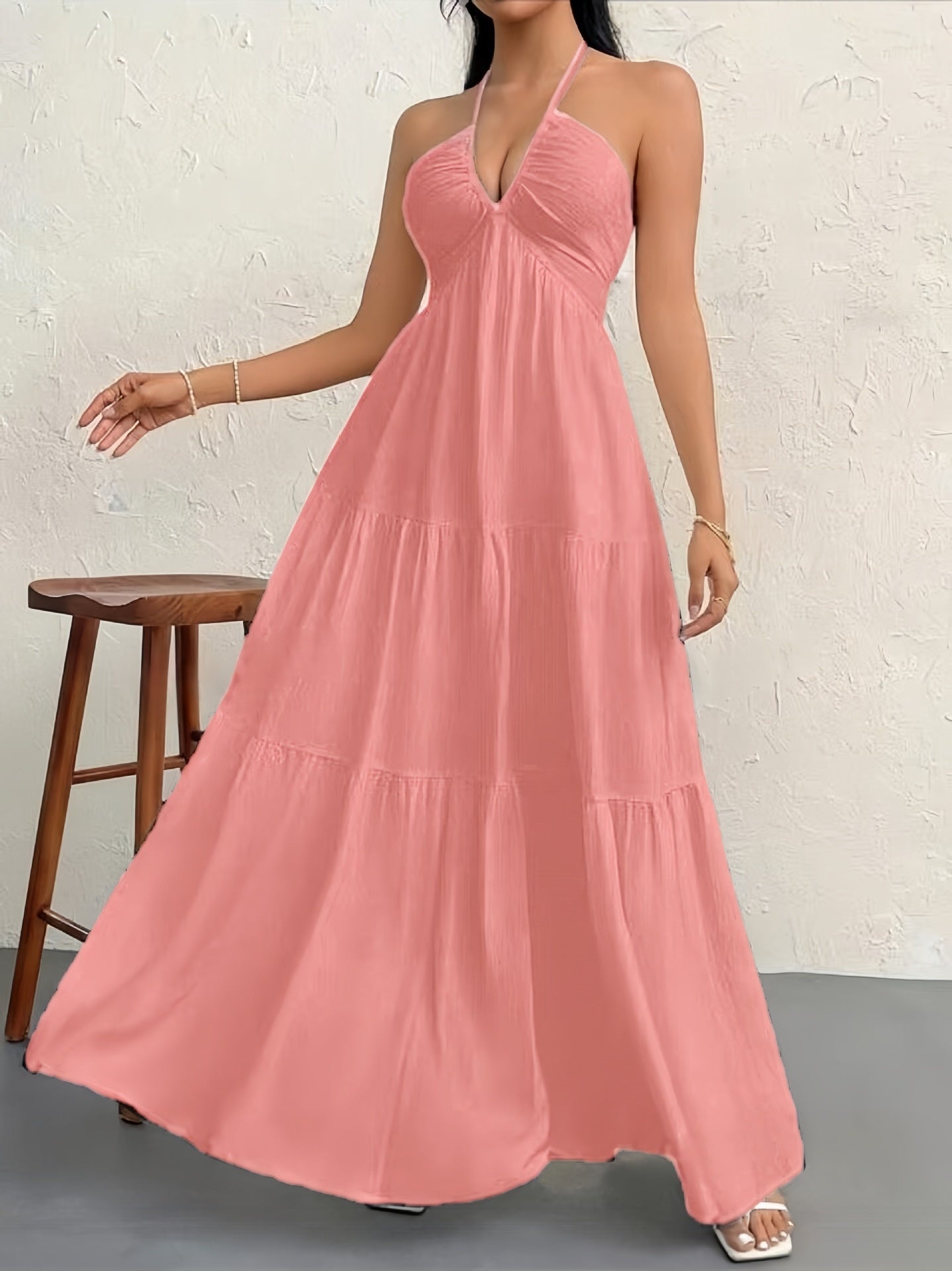 A dusty pink, sleeveless halter maxi dress with a gathered, tiered skirt and a textured, lightweight fabric.