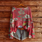 A red, long-sleeve knit sweater with a colorful floral pattern, styled with denim shorts on a wooden background.