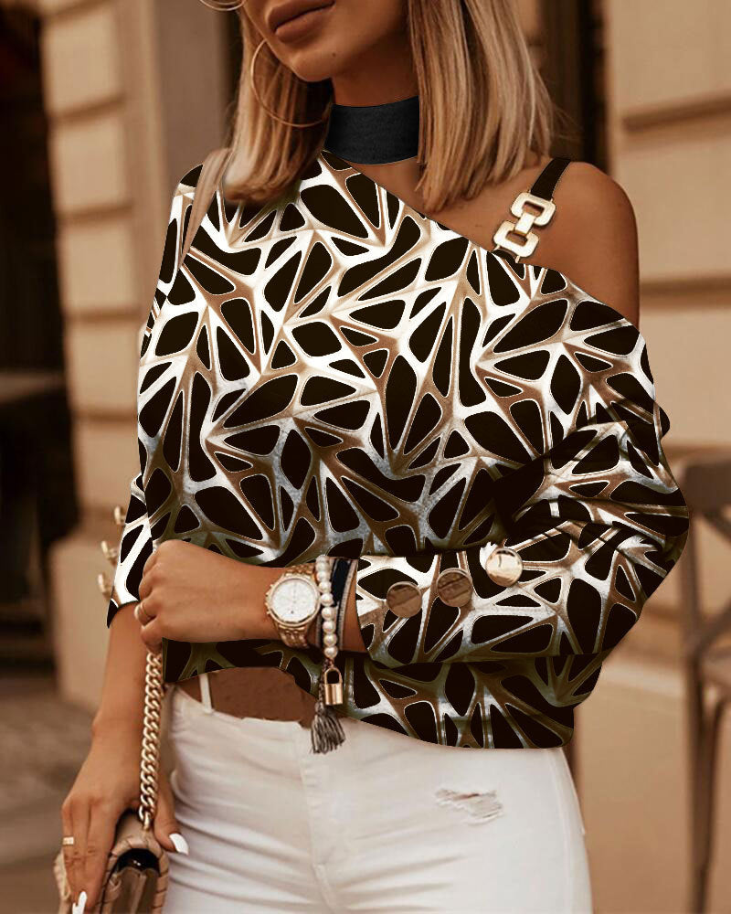 Black and tan geometric print cold-shoulder top with a silver chain link strap, worn with white distressed jeans.