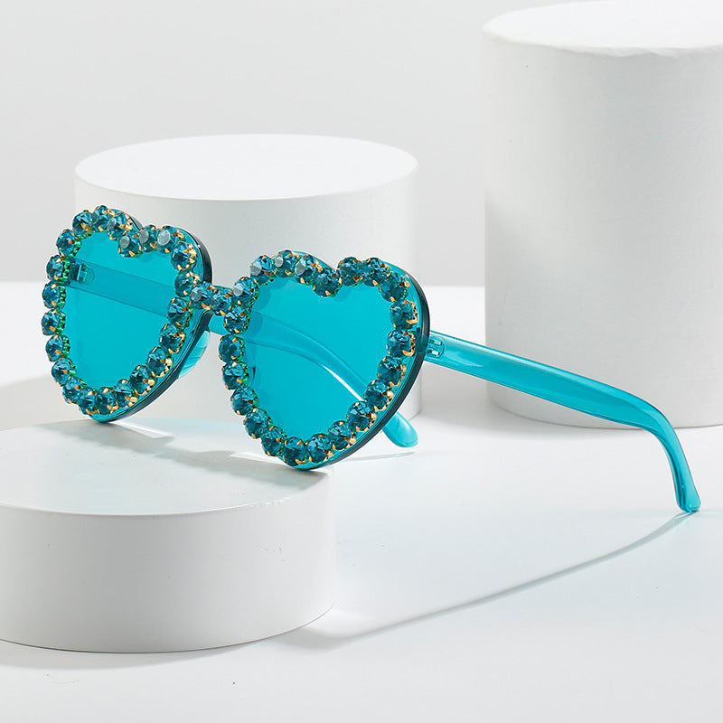 Turquoise heart-shaped sunglasses with matching crystal-encrusted rims, displayed on white pedestals.