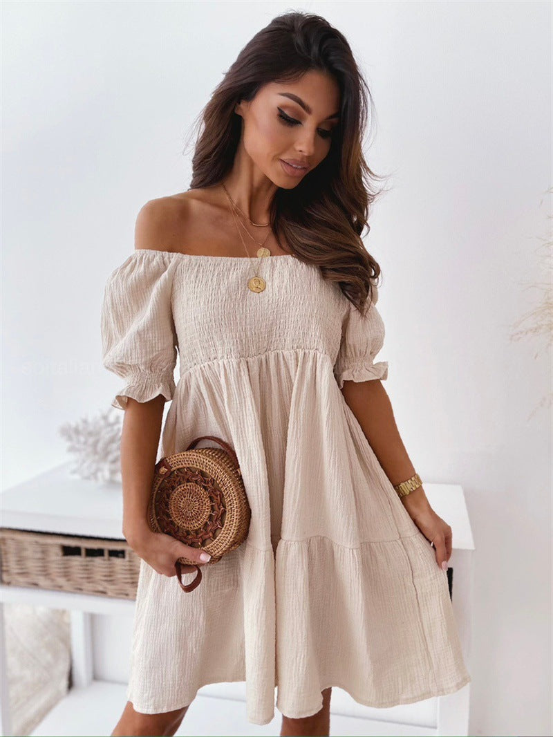 Woman wearing a beige, off-the-shoulder, smocked mini dress with puff sleeves, holding a round woven straw bag.