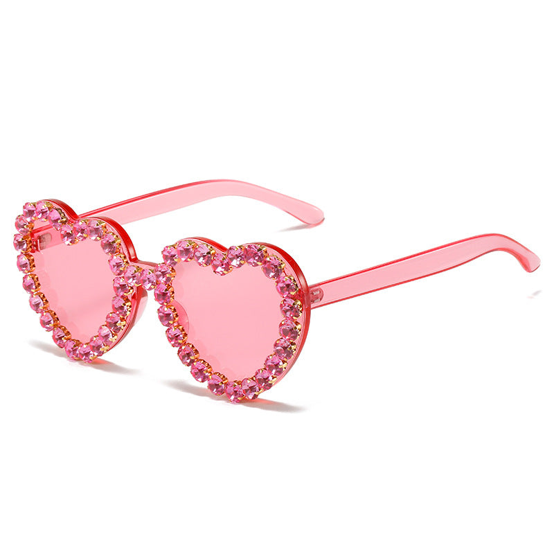 Pink heart-shaped sunglasses with translucent frames and a sparkling rim of pink rhinestone crystals.