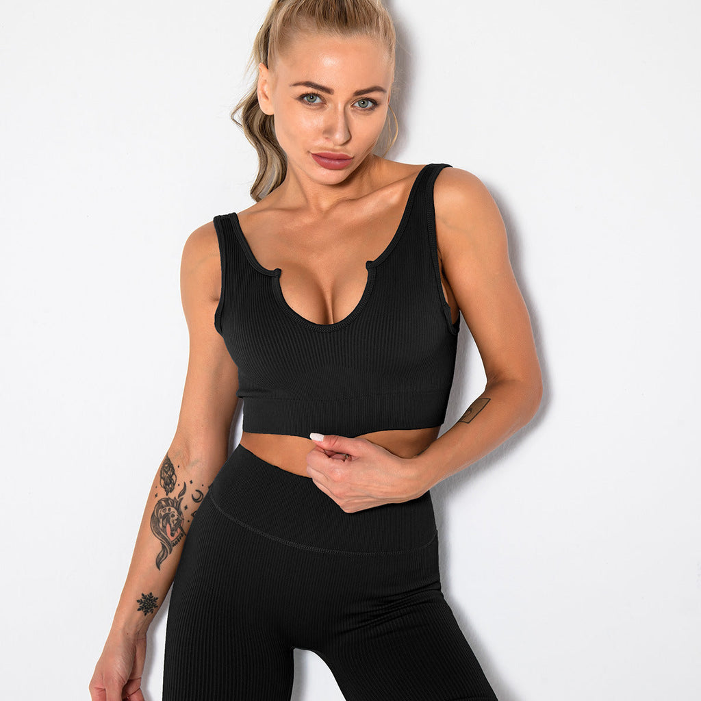 Woman wearing a black ribbed sports bra with a front cutout neckline and matching high-waisted leggings.