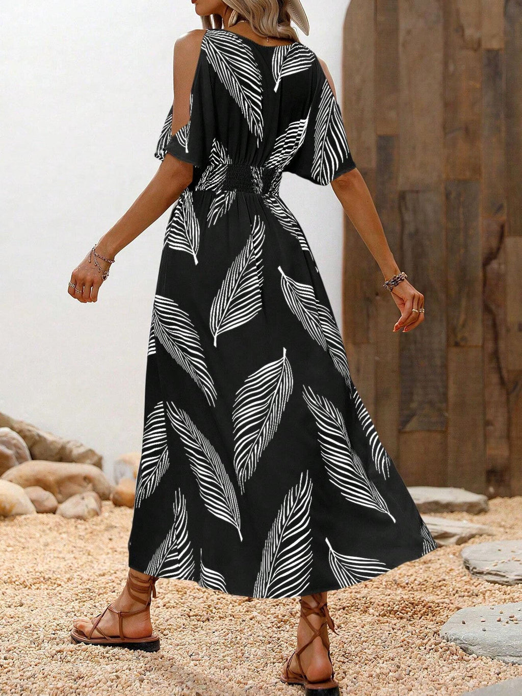 Back view of a black midi dress with white leaf print, cold-shoulder sleeves, and a smocked, elasticized waist.