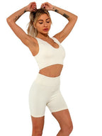 A woman wearing a cream, ribbed seamless workout set consisting of a sports bra and high-waisted biker shorts.