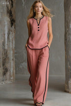 A woman wears a dusty pink, sleeveless matching set with black trim details and button accents on the top.