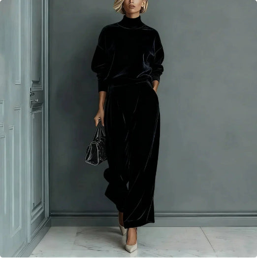 A woman wears a black velour long-sleeve high-neck top and matching wide-leg pants, holding a black handbag.