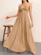 A tan, floor-length tiered maxi dress with a halter neckline and gathered bodice in textured, lightweight fabric.
