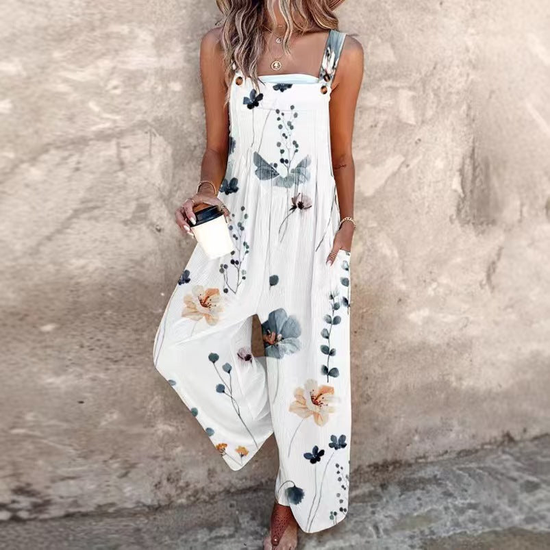 White wide-leg jumpsuit with blue and yellow floral print, featuring buttoned straps and side pockets.