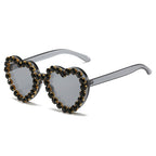 Heart-shaped sunglasses with translucent grey frames and decorative black rhinestone embellishments around the lenses.
