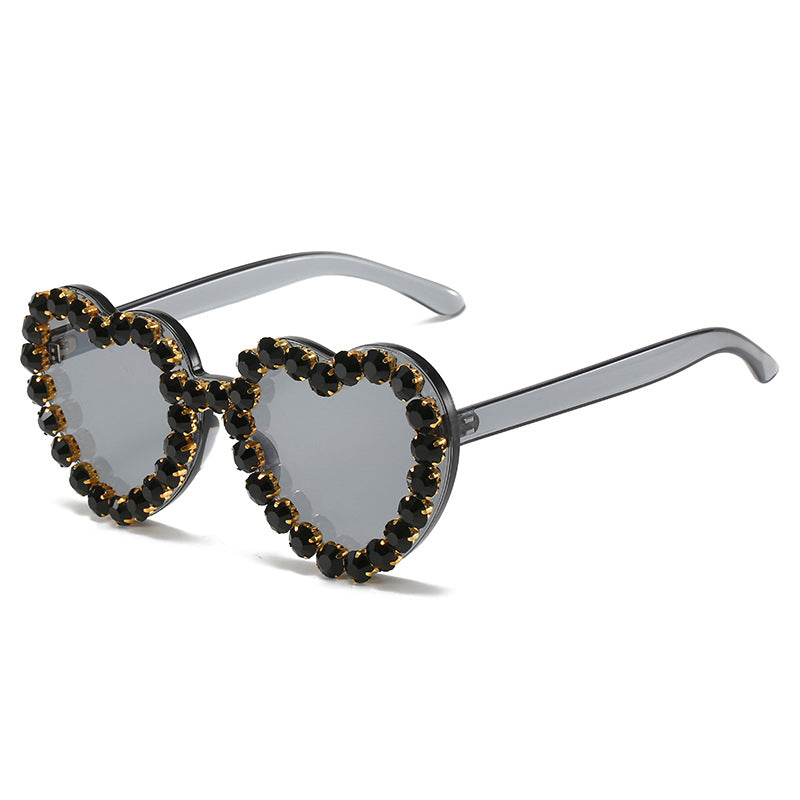 Heart-shaped sunglasses with translucent grey frames and decorative black rhinestone embellishments around the lenses.