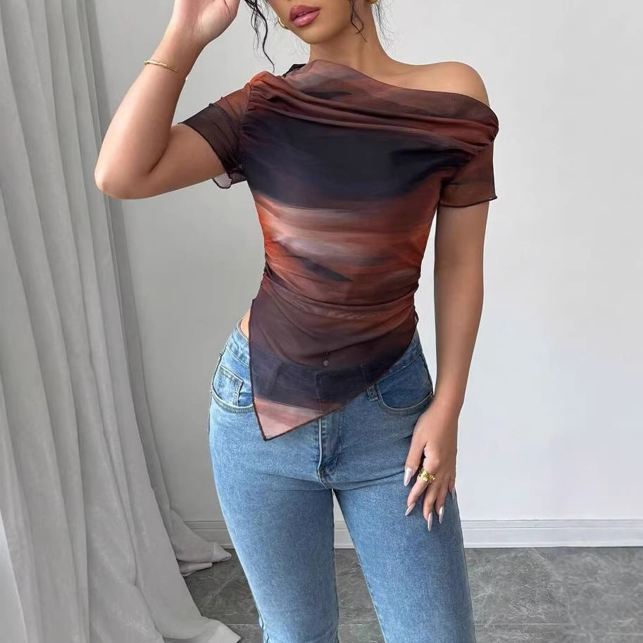 Woman wearing a sheer, off-shoulder short-sleeve top with a brown and black abstract print and asymmetrical hem.