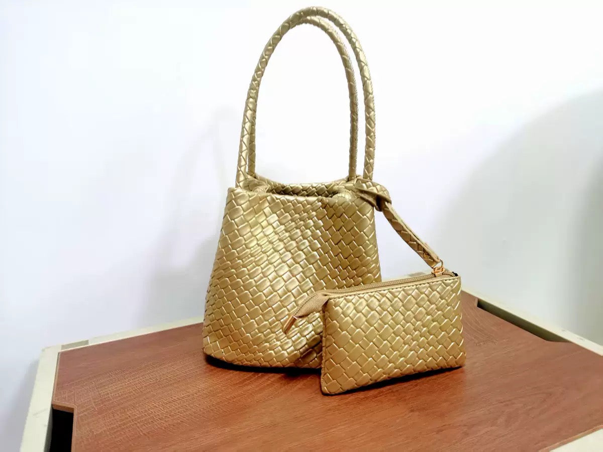 Metallic gold woven leather bucket bag and matching rectangular zippered pouch on a wood surface.