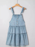 Women’s tiered flowy denim overall dress with raw hem made of 100% cotton, featuring adjustable straps and a relaxed fit.