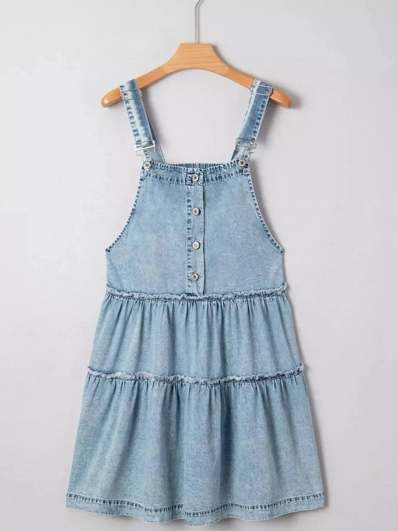 Women’s tiered flowy denim overall dress with raw hem made of 100% cotton, featuring adjustable straps and a relaxed fit.