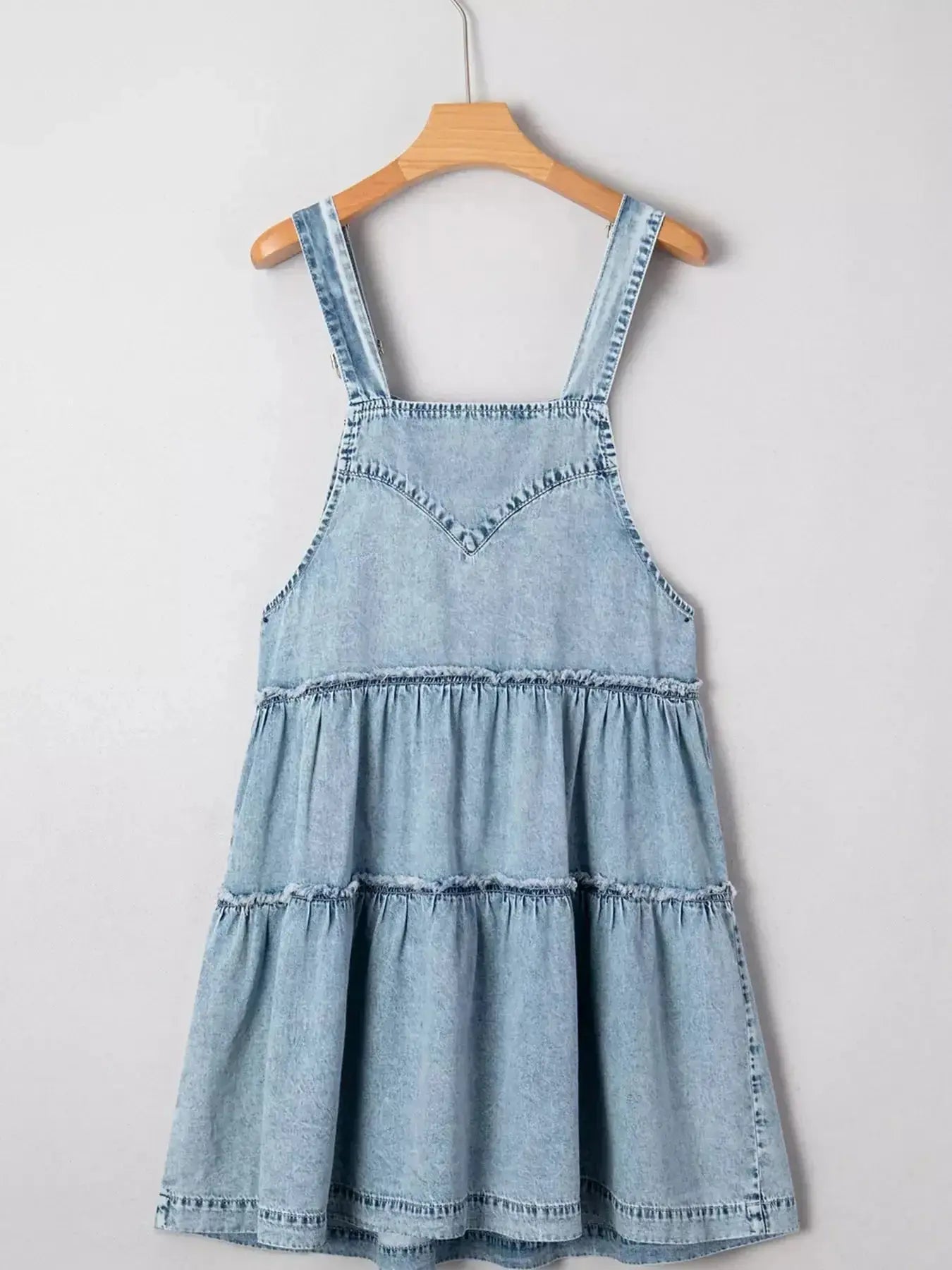 Women’s tiered flowy denim overall dress with raw hem, 100% cotton, by Trendsi, shown on a model in a casual outdoor setting.