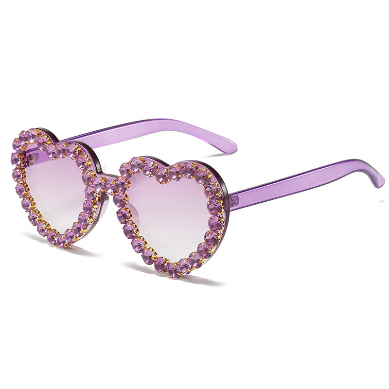 Purple heart-shaped sunglasses with light purple gradient lenses and rhinestone-encrusted frames.