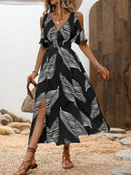 A woman wears a black, cold-shoulder midi dress with a white feather pattern, V-neck, and a high leg slit.