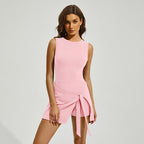 A woman models a light pink sleeveless romper with a wrap-style skort overlay and a side tie waist.