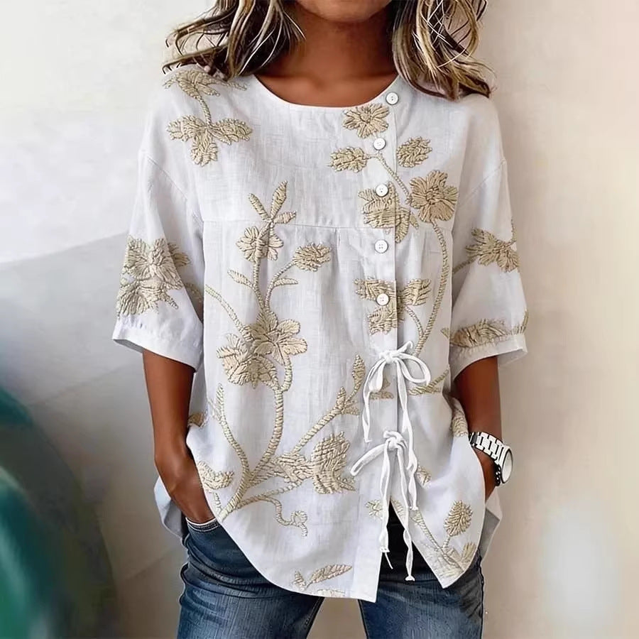 White linen-blend blouse with beige floral embroidery, button front, and decorative side ties.