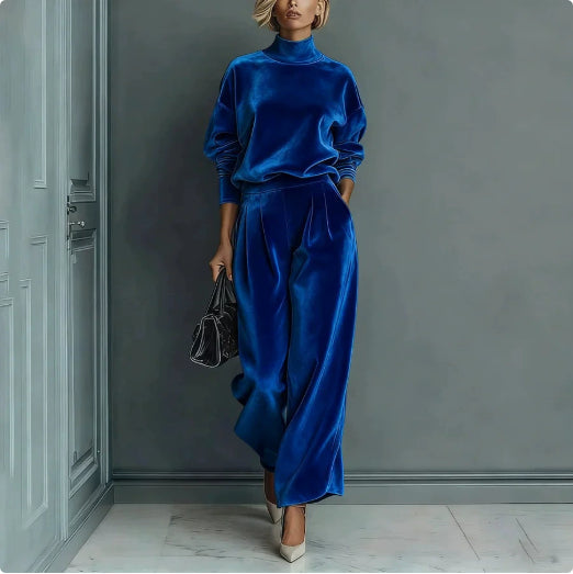 A woman wears a royal blue velour high-neck long-sleeve top and matching wide-leg pants, holding a black handbag.