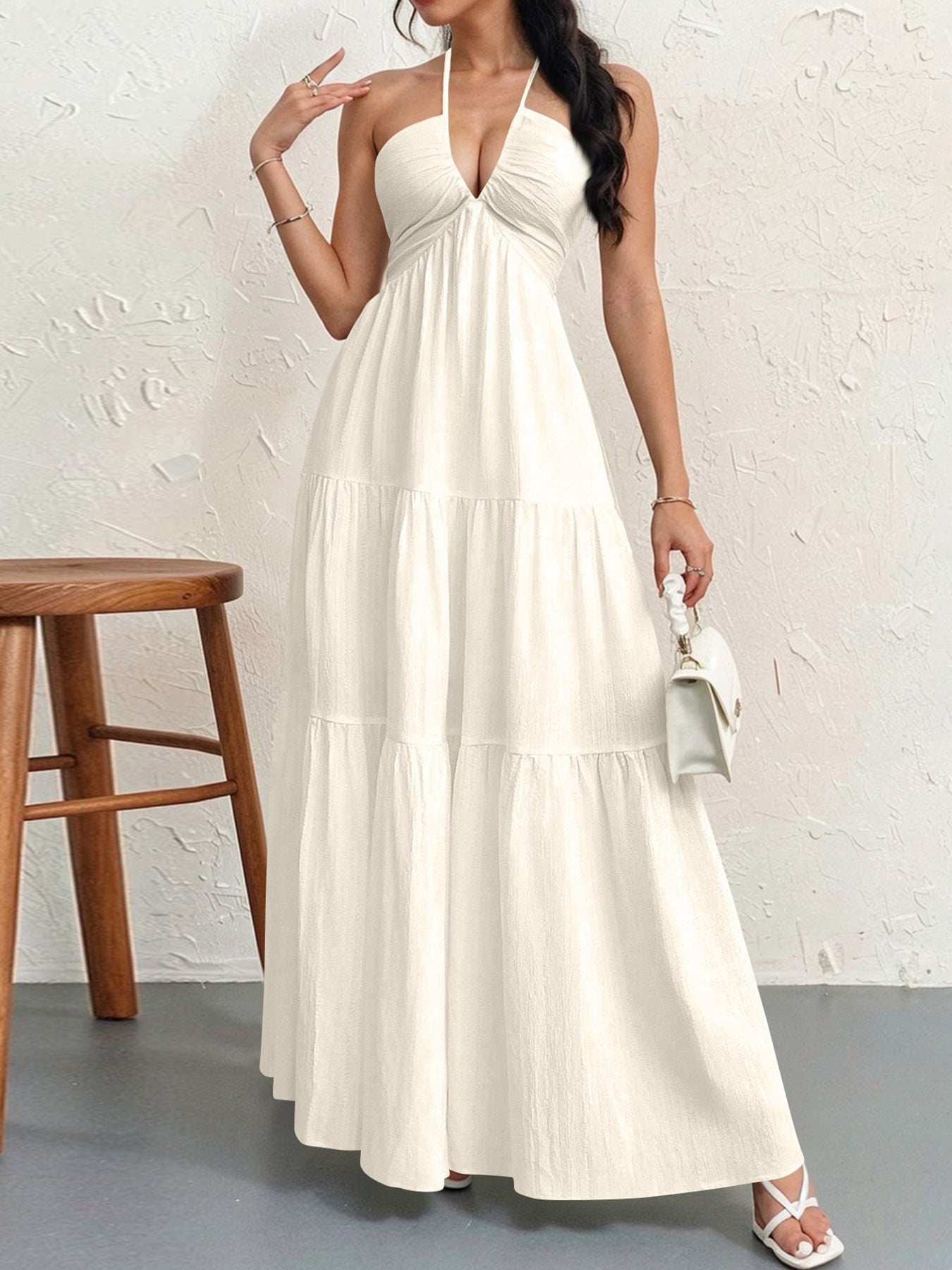 A white tiered maxi dress with a halter neckline, worn with a small white handbag and white strappy sandals.