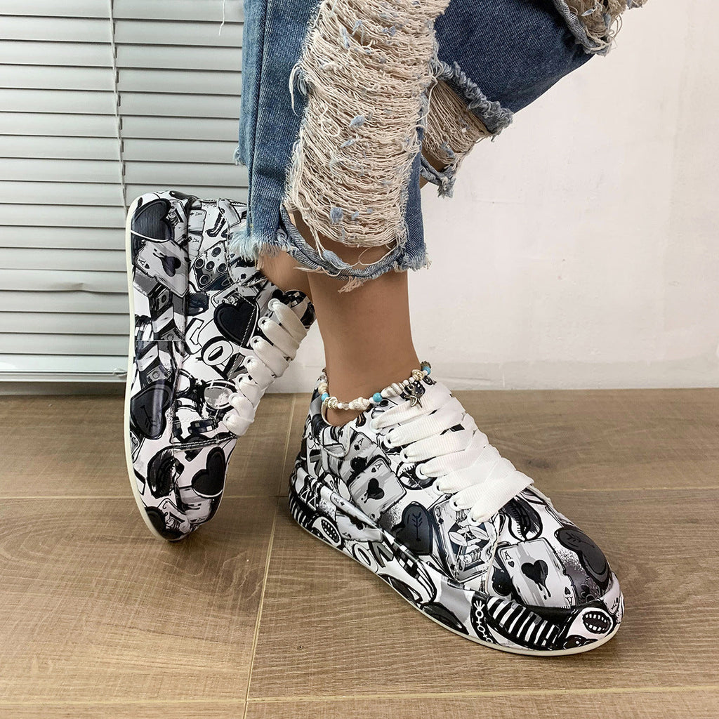 White lace-up sneakers featuring a black and white graphic playing card and heart print, worn with distressed jeans.
