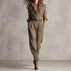 A woman models a brown plaid-print long-sleeve jumpsuit with a button-up top, chest pockets, and a brown leather belt.