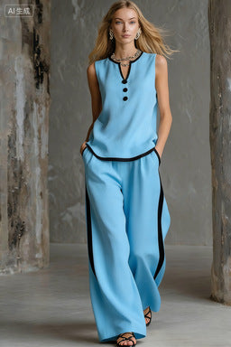 A woman wears a light blue sleeveless top and matching wide-leg pants with black piping and button details.