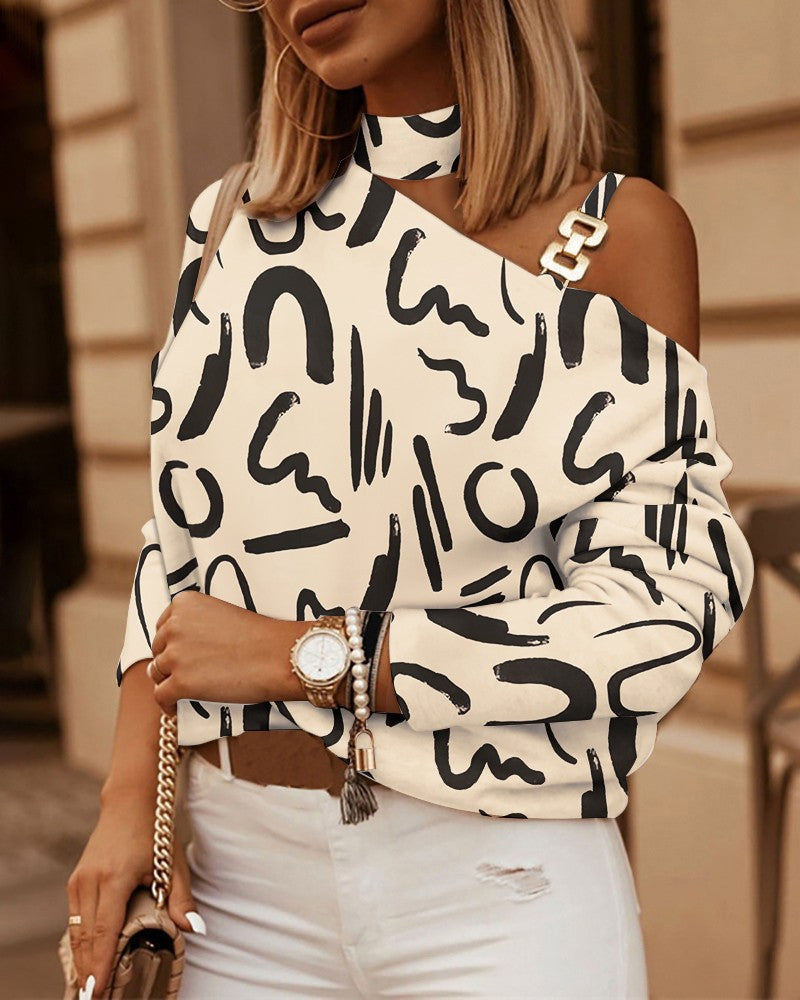 Cream and black abstract-print, one-shoulder top with a choker neck and gold chain link strap detail.
