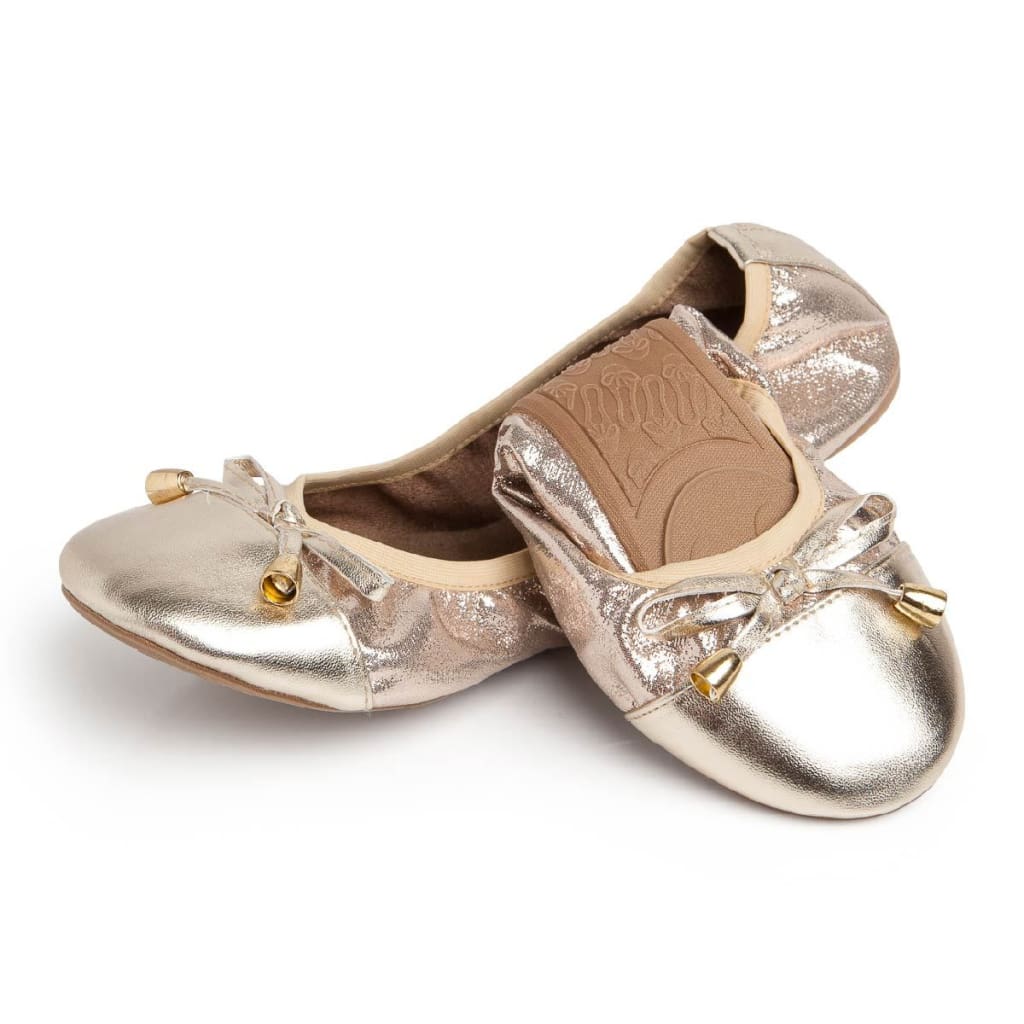 Metallic champagne ballet flats with a bow detail and gold-toned metal tips, featuring a textured finish.